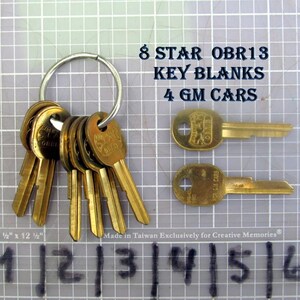 May include: A collection of brass key blanks on a silver ring, with two individual keys displayed. Text reads "8 STAR OBR13 KEY BLANKS 4 GM CARS." The keys are on a grid background with measurements in inches.