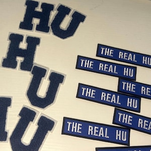 May include: Six blue and white felt patches with the letters "HU" in a variety of sizes and styles.  Five blue and white rectangular patches with the text "THE REAL HU" in white.