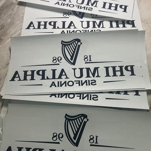 May include: A stack of white signs with black text and a black harp logo. The text reads "80 81 AHIJA UM IHI AIMONO".