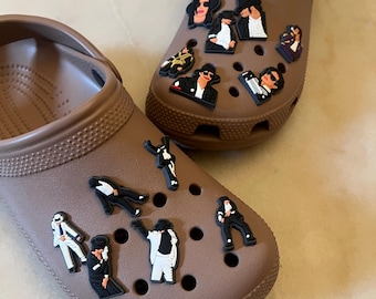 May include: Two brown clogs decorated with various black and white character charms. The charms depict a famous musician in different poses and outfits. The clogs are made of a rubbery material.