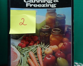 May include: A vintage cookbook titled "Home Canning & Freezing" with a yellow sticky note on the cover that says "2". The cover features a photo of jars of preserved food, fresh produce, and a piece of meat.