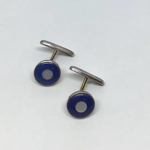 Puede incluir: Un par de gemelos de plata con un diseño de esmalte azul y blanco. Los gemelos son redondos con un centro blanco y un anillo exterior azul.