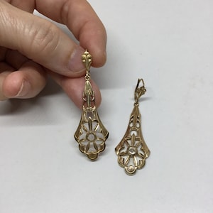 May include: A pair of gold dangle earrings with a delicate floral design and a clear stone in the center of each flower.