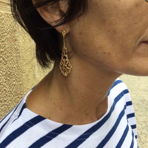 May include: Gold dangle earrings with a delicate, intricate design. The earrings are teardrop shaped and feature a floral pattern.