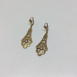 May include: A pair of gold dangle earrings with a floral design and a clear stone in the center of each flower.