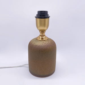 May include: A ceramic table lamp base with a textured, mottled brown and green finish. The lamp features a brass-colored metal neck and a black lamp socket. A gray electrical cord extends from the base.