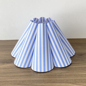 May include: A lampshade featuring a series of vertical, cone-shaped panels arranged in a circular pattern. Each panel displays a repeating pattern of light blue and white vertical stripes, creating a pleated, scalloped appearance around the top.