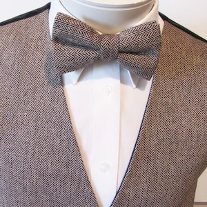 Könnte beinhalten: Eine braune und schwarze Weste mit Fischgrätenmuster und einer passenden Fliege. Die Weste hat einen dunkelblauen Saum an den Rändern.