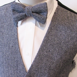 Könnte beinhalten: Eine schwarze und weiße Weste mit Fischgrätenmuster und einer passenden Fliege. Die Weste hat einen V-Ausschnitt und ist aus einem strukturierten Stoff gefertigt.