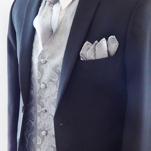 May include: A dark grey suit jacket with a white dress shirt, a silver paisley waistcoat, and a matching tie. A silver pocket square is in the breast pocket. The suit is displayed on a mannequin.