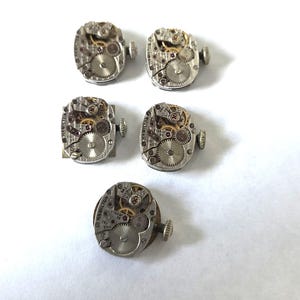 May include: Five vintage Hamilton watch movements. The movements are silver-toned with visible gears, jewels, and other internal components. Each movement has a small crown and is set against a white background. The watch movements are likely for repair or restoration.