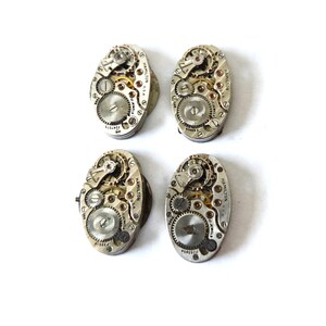 May include: Four vintage Hamilton watch movements, showcasing intricate gears and mechanisms. Each oval-shaped piece features silver-toned metal and visible components, with text indicating "Hamilton U.S.A." and "17 Jewels".