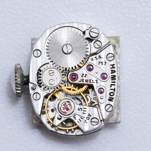 May include: Close-up of a vintage Hamilton watch movement. The silver-toned mechanism features intricate gears, ruby jewels, and the text "U.S.A. 757" and "22 Jewels". The watch has a silver-toned winding stem.