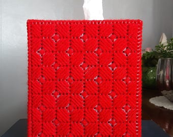 May include: Red crocheted tissue box cover with a diamond pattern. The cover is sitting on top of a blue book.