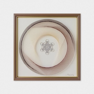 May include: A framed string art piece with a geometric design in the center. The design is made of brown and white string and is surrounded by a circle of white beads. The frame is brown with a gold trim.