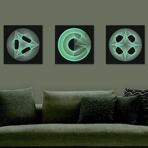 May include: Three framed black and white geometric designs with a glowing green outline. The designs are displayed on a wall above a gray couch with pillows.