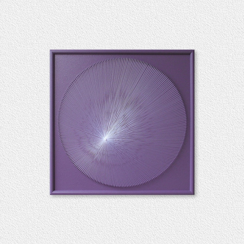 May include: A framed artwork with a purple background and a white circular design in the centre. The design is made up of thin lines radiating outwards from the centre.