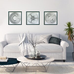 Puede incluir: Tres piezas de arte de pared enmarcadas en negro con dise&ntilde;os geom&eacute;tricos abstractos en blanco sobre una pared blanca por encima de un sof&aacute; blanco con una manta y almohadas.