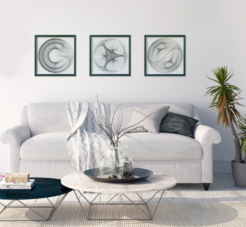 Puede incluir: Tres piezas de arte de pared enmarcadas en negro con dise&ntilde;os geom&eacute;tricos abstractos en blanco sobre una pared blanca por encima de un sof&aacute; blanco con una manta y almohadas.