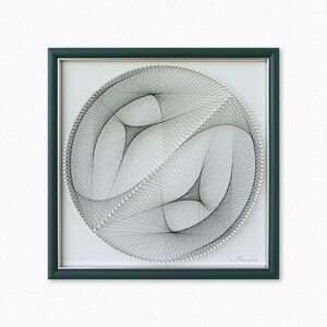 Puede incluir: Una pieza de arte de hilo enmarcada con un dise&ntilde;o en blanco y negro de dos c&iacute;rculos superpuestos. El dise&ntilde;o se crea con hilo envuelto alrededor de clavos en un patr&oacute;n circular. El marco es de color verde oscuro.