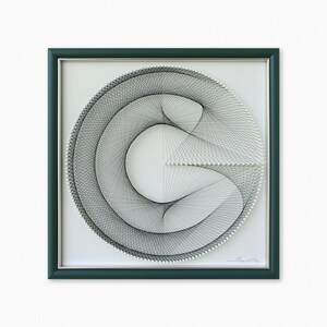Puede incluir: Una obra de arte enmarcada que presenta un dise&ntilde;o de arte de hilo negro y blanco de un c&iacute;rculo con una l&iacute;nea curva en su interior. El marco es de color verde oscuro.