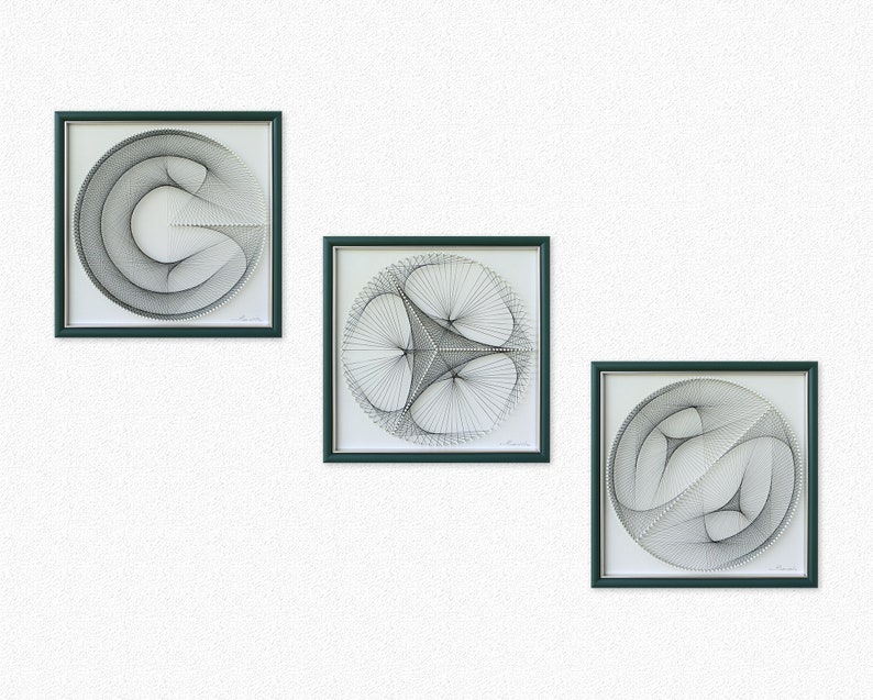 Puede incluir: Tres piezas de arte de hilo en blanco y negro enmarcadas con dise&ntilde;os geom&eacute;tricos. Los marcos son de color verde oscuro.