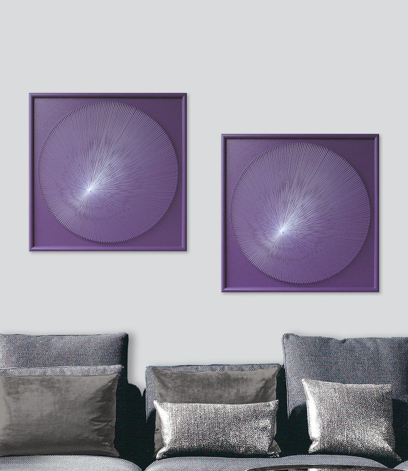 May include: Two square framed wall art pieces with a purple background and a white circular design in the centre. The design is made of thin lines radiating from the centre.