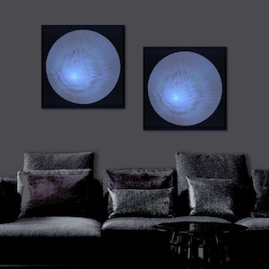 May include: Two black framed wall art pieces with a white, circular design on a dark grey wall above a black sofa with black cushions.
