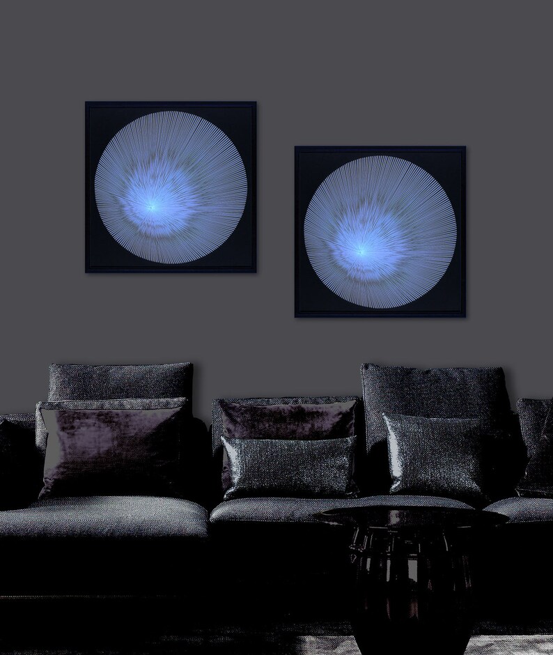 May include: Two black framed wall art pieces with a white, circular design on a dark grey wall above a black sofa with black cushions.