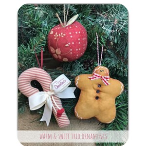 Può includere: Tre addobbi natalizi fatti a mano: una mela rossa, un omino di pan di zenzero e una canna di zucchero. Gli addobbi sono appesi a un albero di Natale verde.