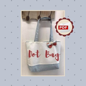 May include: A white tote bag with small gray polka dots and a denim blue base and handles. The words "Dot Bag" are written in red script across the front. A red bow is attached to the top of the bag. A PDF icon is in the upper right corner.