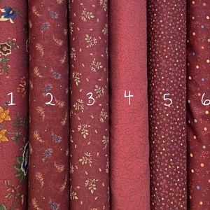 Può includere: Sei campioni di tessuto in varie tonalità di bordeaux con diversi motivi, tra cui disegni floreali, a foglia e geometrici. I campioni sono numerati da 1 a 6.