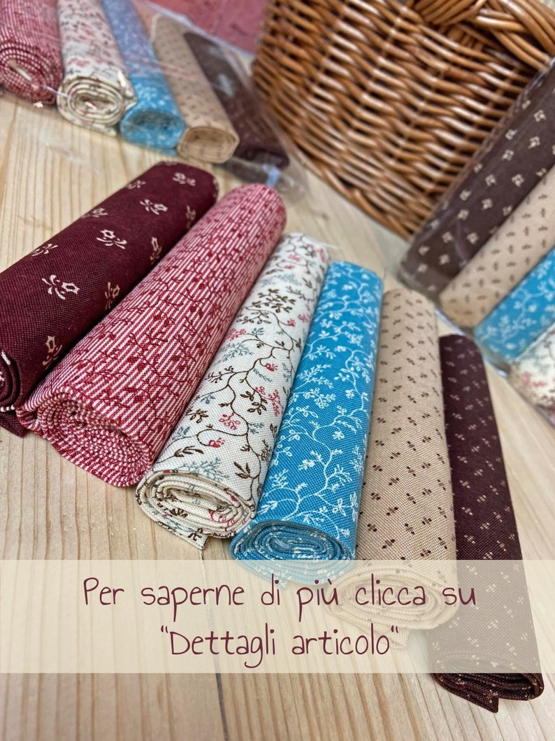 Pode incluir: Uma cole&ccedil;&atilde;o de rolos de tecido em v&aacute;rios padr&otilde;es e cores, incluindo vermelho, marrom, bege e azul. Os rolos de tecido est&atilde;o dispostos em uma pilha sobre uma superf&iacute;cie de madeira. O texto "Per saperne di pi&ugrave; clicca su "Dettagli articolo"" &eacute; vis&iacute;vel na parte inferior da imagem.
