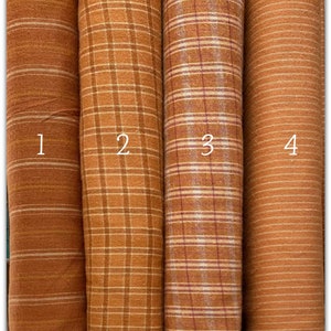 Può includere: Quattro campioni di tessuto in diversi motivi. I campioni sono tutti in tonalità di marrone e arancione. Il primo campione ha un motivo a strisce sottili, il secondo ha un motivo a quadri, il terzo ha un motivo a quadri con una striscia rossa e il quarto ha un motivo a strisce sottili.