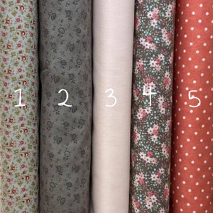 Può includere: Cinque campioni di tessuto, numerati da 1 a 5. I campioni sono disposti da sinistra a destra. Il primo campione è un tessuto verde chiaro con un piccolo motivo floreale. Il secondo campione è un tessuto grigio scuro con un piccolo motivo floreale. Il terzo campione è un tessuto beige chiaro. Il quarto campione è un tessuto grigio scuro con un piccolo motivo floreale rosa e blu. Il quinto campione è un tessuto rosso con pois bianchi.