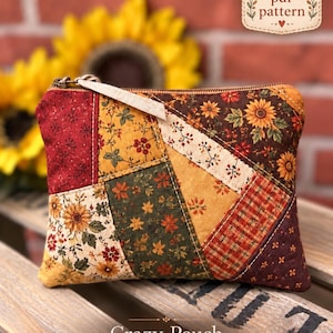 Puede incluir: Un estuche de tela rectangular con un diseño de patchwork de patrones otoñales en tonos rojos, naranjas, amarillos y verdes. El estuche tiene una cremallera de metal con un tirador de tela clara y está etiquetado como Crazy Pouch.