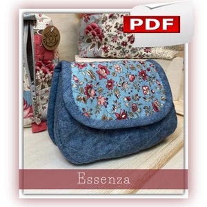 Puede incluir: Un bolso de mano acolchado de estilo denim con solapa floral. La solapa presenta un fondo azul claro con un estampado de flores rosas, rojas y crema. La palabra "Essenza" está impresa en la parte inferior de la imagen. Otros bolsos con estampado floral son visibles en el fondo.