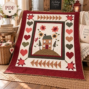 Op de afbeelding: Een rechthoekige quilt met een centrale applicatie van een huis op een heuvel met bloemen en bomen, omringd door een rand van harten en sterren. De quilt heeft een crèmekleurig midden, een donkergroene binnenrand en een brede rode buitenrand.