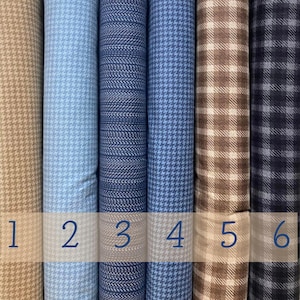 Può includere: Una collezione di rotoli di tessuto con vari motivi e colori. I tessuti includono disegni a pied-de-poule, a spina di pesce e a quadri in tonalità beige, azzurro, blu navy e marrone. Ogni rotolo è numerato da 1 a 6.