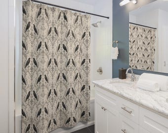 May include: A beige shower curtain with a repeating pattern of black crows and a damask design. The curtain is hanging in a bathroom with white cabinets, a marble countertop, and a dark gray tile floor.