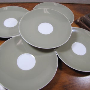 May include: Set of five saucer-shaped plates in a muted green color with a white center circle. The plates are stacked on top of each other.