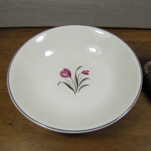 May include: A white ceramic bowl with a blue rim and a pink floral design. The bowl is on a wooden surface.
