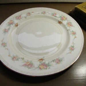 May include: A white ceramic dinner plate with a gold rim and a floral design featuring pink, yellow, and green flowers.