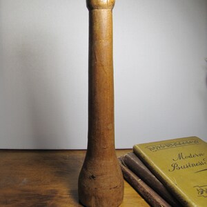 May include: A wooden mallet with a rounded head and a long, slender handle. The mallet is made of light brown wood and has a smooth, polished finish.