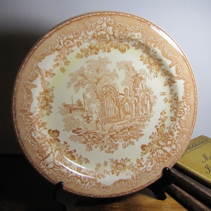 May include: A vintage ceramic plate with a brown and white floral design. The center of the plate features a detailed illustration of a building with a tree in front of it.