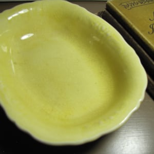 May include: A yellow ceramic bowl with a scalloped edge. The bowl is empty and has a smooth, glossy finish.