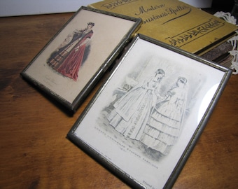 Può includere: Due illustrazioni vintage incorniciate. La prima mostra una donna con un vestito rosso e nero. La seconda mostra due donne con abiti bianchi. Il testo sulla seconda cornice recita "Craddock's Unrivaled Colored Fashions."