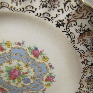 May include: A white ceramic plate with a blue and gold floral design. The plate has a scalloped edge and is decorated with a gold rim.