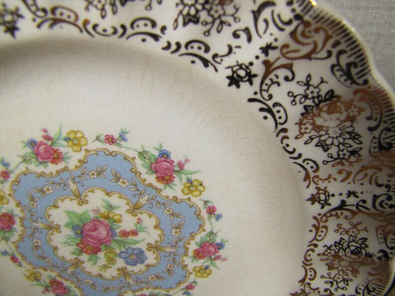 May include: A white ceramic plate with a blue and gold floral design. The plate has a scalloped edge and is decorated with a gold rim.