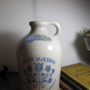 May include: A white ceramic jug with a blue floral design and the text "Henry McKenna Hand Made Kentucky Whiskey, Old Nelson County, Kentucky Since 1855".